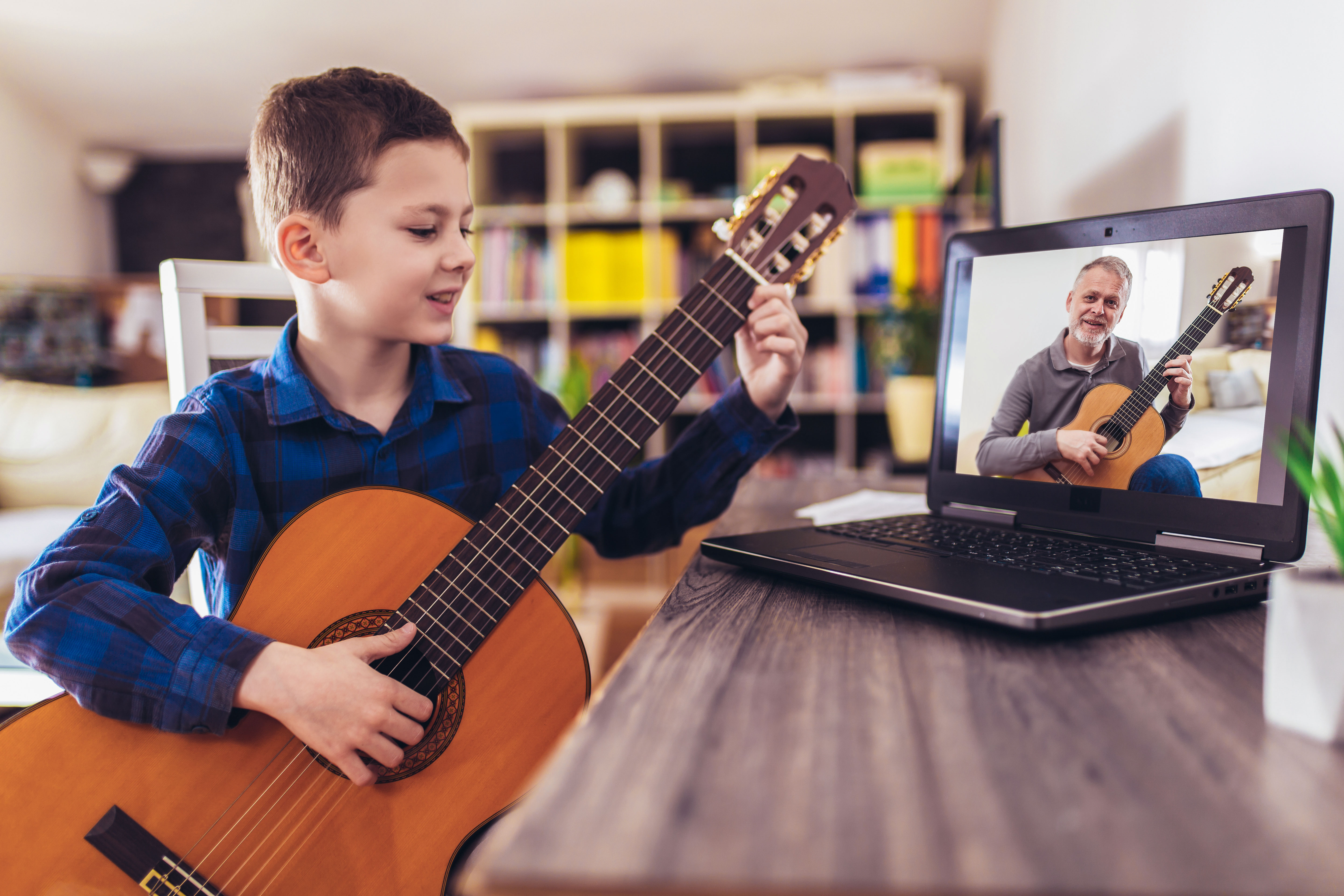 Image of a boy having an online guitar lesson smiling at a laptop